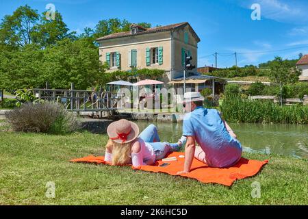 Couple de détente et de lecture sur les rives du Canal du midi devant la maison du gardien de l'écluse transformée en un restaurant et lit et petit déjeuner ca Banque D'Images