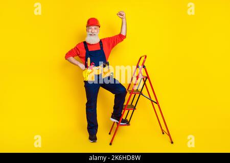 Photo pleine longueur de retraité ouvrier lever bras vers le haut réparation maison avec l'échelle d'équipement isolé sur fond de couleur vive Banque D'Images