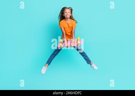 Photo pleine longueur de doux mignon petit enfant porter orange t-shirt montant longboard jumping haut isolé turquoise couleur fond Banque D'Images