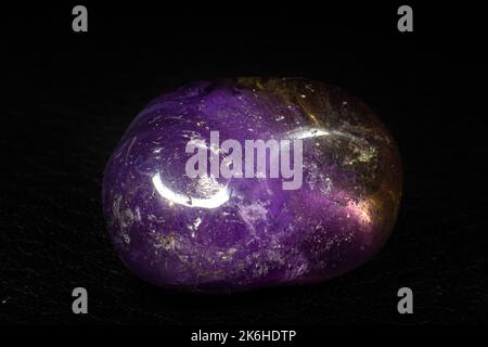 Macro en pierre d'Amétrine tumillée réelle isolée sur une surface noire. Cristal violet avec un peu de coloration jaune à l'extrémité Banque D'Images