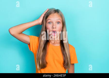 Gros plan photo de jeune fille adorable drôle écolière enfant porter t-shirt orange bouche ouverte tête de contact inattendue peur isolée sur fond bleu-vert Banque D'Images