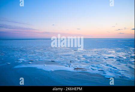 Vue aérienne - deux personnes marchent sur la glace au coucher du soleil sur la mer gelée. Paysage hivernal sur la mer au crépuscule. Vue depuis le dessus de la fonte de glace dans l'océan Banque D'Images