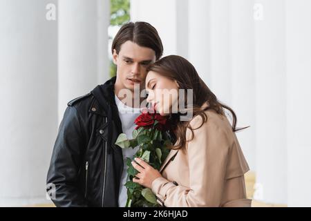 jolie jeune femme sentant des roses rouges près de l'élégant petit ami dans la veste, image de stock Banque D'Images