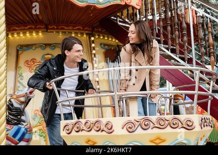 couple gai en tenues automnales regardant d'autres sur le carrousel dans le parc d'attractions, image de stock Banque D'Images