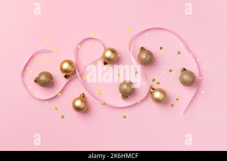 Carte de Noël avec boules dorées à paillettes, confetti en forme de coeur et ruban de satin sur fond rose avec lumières floues bokeh Banque D'Images