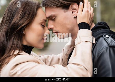 vue latérale de la femme souriante en trench beige qui embrasse le petit ami, image de stock Banque D'Images