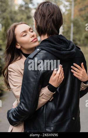 jeune et jolie femme en manteau embrassant petit ami dans la veste noire, image de stock Banque D'Images