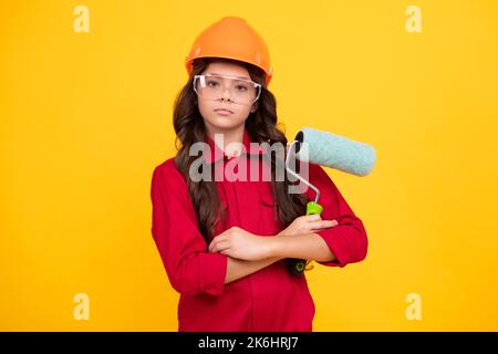 Petit expert en casque de constructeur sur le chantier de construction. Peintre de fille ado avec outil de pinceau ou rouleau de peinture. Enfant sur le travail de réparation. Rénovation Banque D'Images