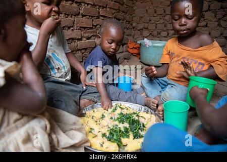 Un groupe d'enfants africains mangent un repas de bananes et de légumes verts avec sauce aux arachides à l'intérieur de leur maison dans le district de Kasese, en Ouganda, en Afrique de l'est. Banque D'Images