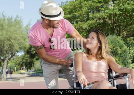 beau homme poussant belle femme en fauteuil roulant dans le parc Banque D'Images