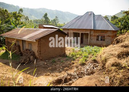 Une maison en briques améliorée avec une nouvelle tôle et un petit panneau solaire se trouve devant une ancienne maison construite dans la boue dans le district de Kasese, en Ouganda, en Afrique de l'est. Banque D'Images