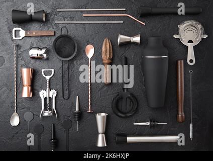 Divers ustensiles de bar à cocktails. Passoire,shaker,jigger,paille,presse-fruits,presse-boue,ouvre-vin sur fond de pierre noire.vue du dessus. Banque D'Images