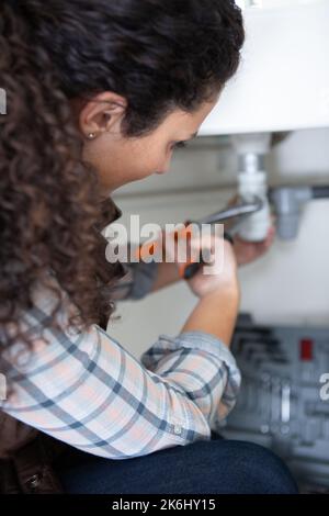 une femme qui fixe l'évier de cuisine Banque D'Images