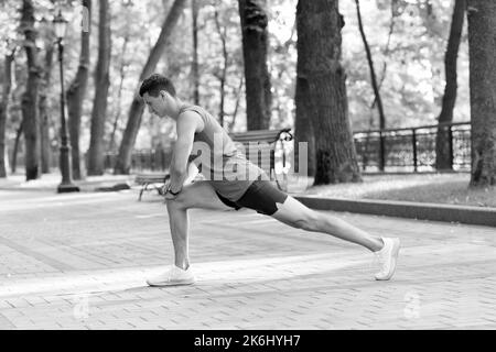 Sportsman tenir la position de fente faire une routine d'étirement pendant l'entraînement sportif en plein air dans le parc, l'échauffement. Banque D'Images