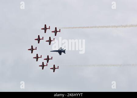 Snowbirds de l'ARC volant en formation, avec un avion de chasse. Deux flux de fumée de chaque côté de la formation. Banque D'Images