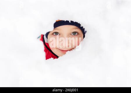 Garçon regarde à travers un trou dans le mur d'un château de neige. Garçon joue avec la neige Banque D'Images