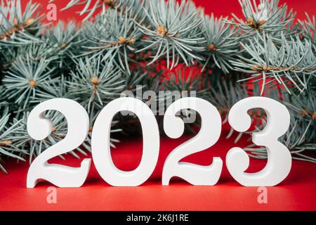 Bonne année 2023. Support en bois blanc numéros 2023 avec branches de Noël vertes et luxuriantes sur fond rouge. Joyeux Noël. Banque D'Images