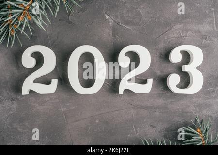 Bonne année 2023. Le bois blanc n° 2023 se trouve sur une surface en béton gris et inégal avec des branches d'arbres de Noël. Joyeux Noël. Vue de dessus Banque D'Images