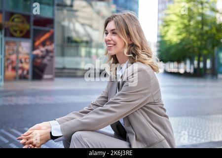 Une femme d'affaires sourit comme assise au centre-ville, porte un costume beige pour le travail de bureau Banque D'Images