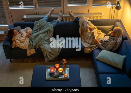 Image symbolique économie d'énergie, hiver froid, crise d'énergie, plat froid, mère et fille couchée, chaudement vêtue sur le canapé, bougie, chauffage sur un Banque D'Images
