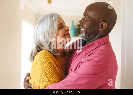 Joyeux couple de personnes âgées et diverses qui se embrassent et se sourient à la maison Banque D'Images