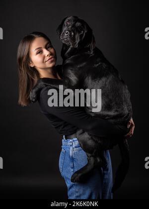 Une fille tient un chien Labrador Retriever dans ses bras. Prise en gros plan dans un studio photo, sur fond noir. Banque D'Images