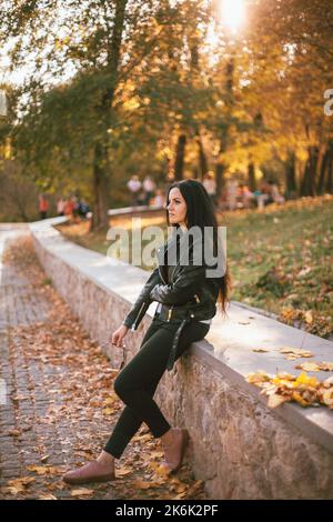 Portrait d'une femme triste et réfléchie portant une veste en cuir debout dans le parc pendant le temps ensoleillé en automne Banque D'Images