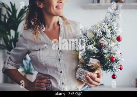Portrait de la femme heureuse sourire et tenir le petit arbre de noël pour décorer la maison pendant les vacances de décembre santa clas Noël saison. Appartement en arrière-plan. Banque D'Images