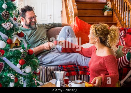 Un couple de jeunes adultes heureux à la maison appréciant le matin de noël en décembre prenant le café et le petit déjeuner ensemble. L'homme sourit à une femme en vacances Banque D'Images