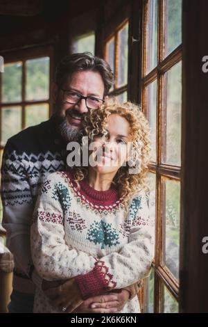 Portrait d'un jeune couple mûr souriant et debout pour une photo, homme et femme portant un pull chaud avec des décorations de noël et de la couleur. Personnes dans Banque D'Images