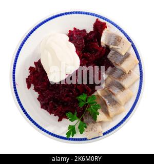 Salade de hareng appétissante avec betteraves, crème sure et persil dans une assiette blanche Banque D'Images