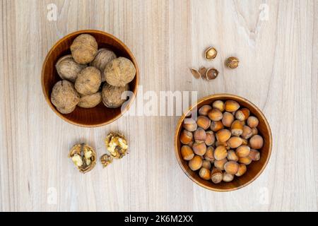 Noisettes et noix dans un bol avec quelques craquelures à côté sur la table. Pose à plat. Banque D'Images