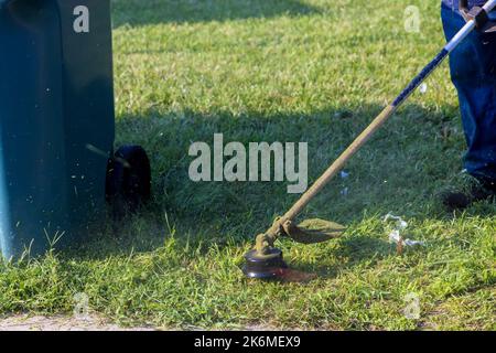 Employé d'un service municipal coupant de l'herbe près du trottoir avec un coupe-herbe à ficelle Banque D'Images