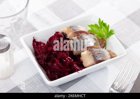Salade de hareng appétissante avec betteraves, crème sure et persil dans une assiette blanche Banque D'Images