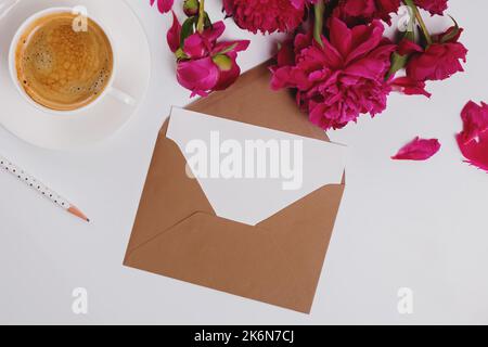 Carte de vœux dans l'enveloppe, plat avec café et pivoines roses, maquette en papier Banque D'Images