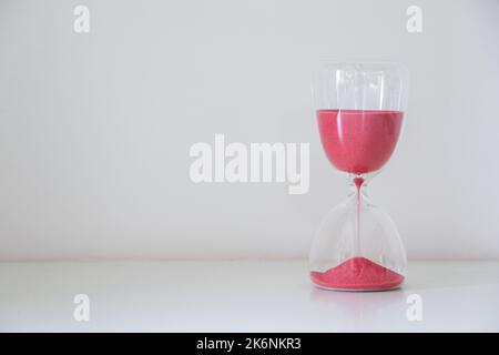 Sable rouge courant à travers les ampoules d'un sablier, isolé à droite de fond blanc, mesurant le passage du temps, compte à rebours jusqu'à une date limite, tim Banque D'Images