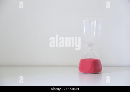 Un sablier isolé à droite du fond blanc, avec tout le sable rouge glissé vers l'ampoule inférieure, ce qui signifie qu'il ne reste plus de temps, le temps a été atteint Banque D'Images