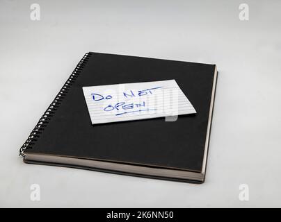 Un livre noir avec une note disant de ne pas ouvrir isolé sur un fond blanc. Banque D'Images