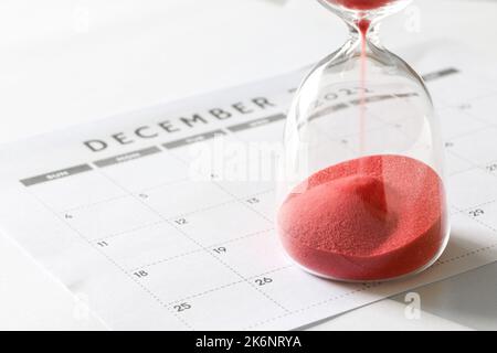 Sable rouge courant à travers des ampoules de sablier, le calendrier de décembre, compte à rebours jusqu'à Noël et la fin de l'année Banque D'Images