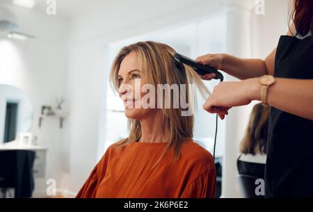 Coiffeur, fer à repasser plat et femme en salon pour un rendez-vous avec un client heureux. Styliste utilisant le lisseur sur le client dans le salon de beauté ou les cheveux Banque D'Images