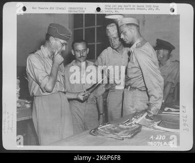 Le commissaire à l'air Sir Arthur Tedder (extrême gauche) étudie les photogrpahs aériens lors de son tour d'inspection à Une base d'escadre de reconstruction photographique en 90th quelque part en Italie sous le nom de Brig. Le général Patrick W. Timberlake (troisième à partir de la gauche) regarde dessus. Banque D'Images