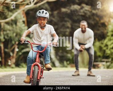 Sur un cheval en acier, je suis à bord. un adorable garçon apprenant à faire du vélo avec son père à l'extérieur. Banque D'Images