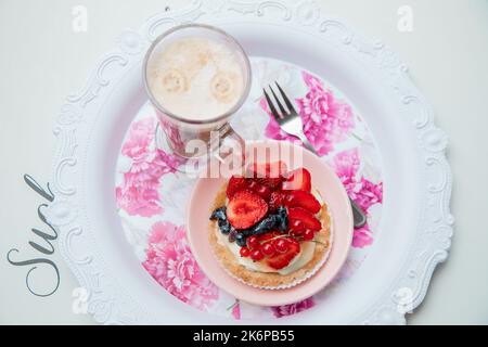 Plateau floral de gâteau crémeux appétissant avec baies fraîches mûres et tasse en verre de café savoureux parfumé avec vue sur le dessus en mousse. Décor élégant Banque D'Images