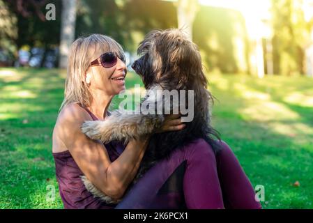 Gros plan d'une femme blonde d'âge moyen avec des lunettes qui câblent son chien berger catalan. Amour pour les animaux. Soin des animaux Banque D'Images