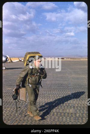 Un pilote transportant son équipement de vol et fumant une cigarette marche par le caméraman. Plusieurs avions F-86 Sabre nord-américains sont en arrière-plan. Un pilote transportant son équipement de vol et fumant une cigarette marche par le caméraman. Plusieurs avions F-86 Sabre nord-américains sont en arrière-plan. Banque D'Images