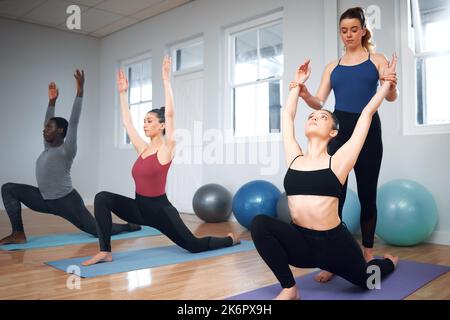 Son mon devoir d'aider. un instructeur de yoga aidant un étudiant à se mettre en position de fente basse. Banque D'Images