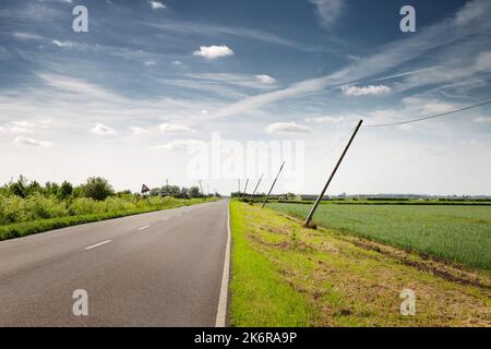 les poteaux téléphoniques se penchent du vent le long d'une route de campagne en angleterre Banque D'Images