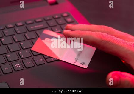 Pirate informatique essayant de voler de l'argent de la carte - la carte bancaire et le clavier d'ordinateur portable sont illuminés par une lumière rouge Banque D'Images