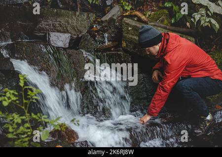 Randonneur sur une longue piste remplit l'eau potable d'une source de montagne dans un récipient en verre. Remplir d'eau propre pour cuisiner et boire tout en étant bien haut Banque D'Images