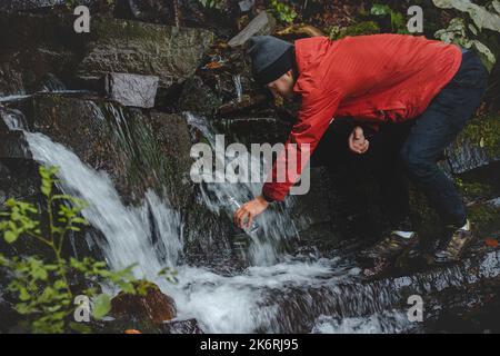 Randonneur sur une longue piste remplit l'eau potable d'une source de montagne dans un récipient en verre. Remplir d'eau propre pour cuisiner et boire tout en étant bien haut Banque D'Images